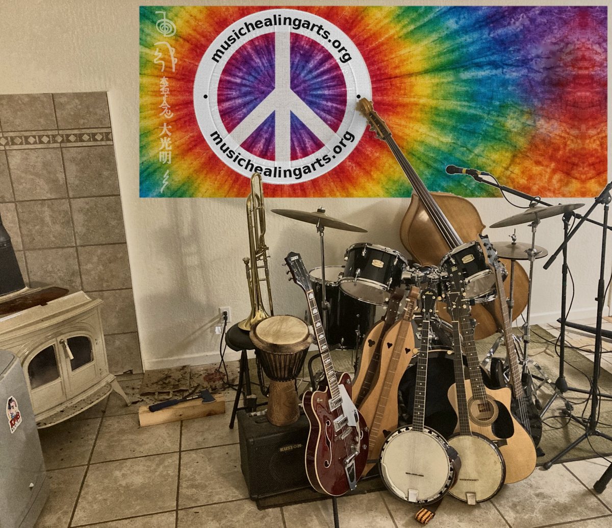 John's music room in Mountain Ranch: drums, upright bass, guitars, banjos, dulcimers, trombone and djembe in front of a tie-dye peace sign tapestry, beside the wood stove